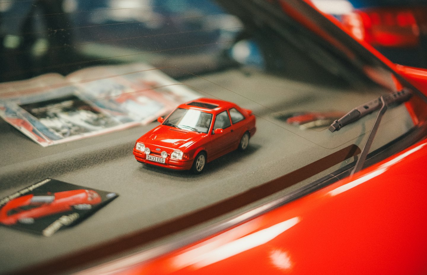 Small red model car parked on a textured grey surface.